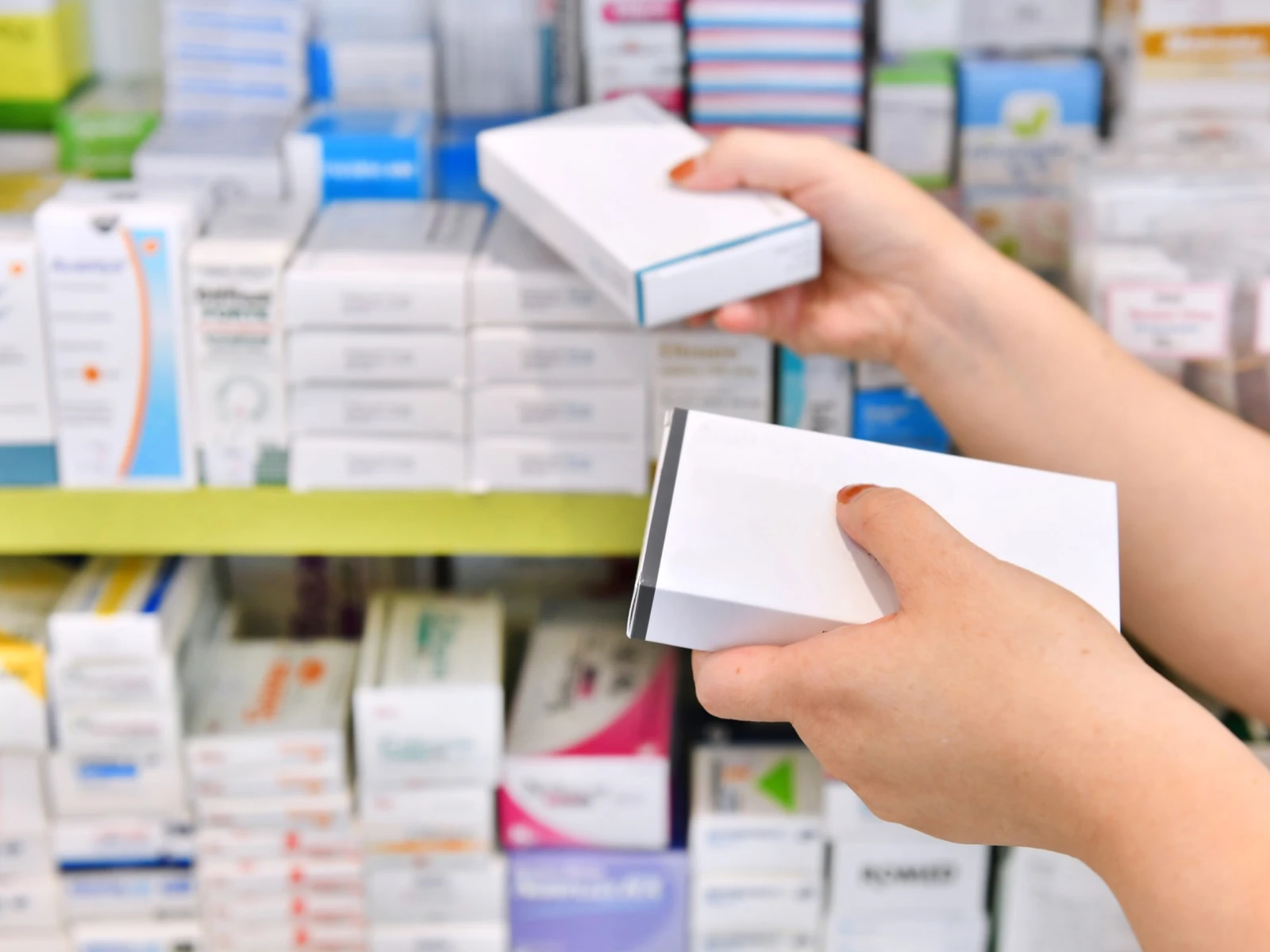 Hands selecting medicine cartons from pharmacy shelves