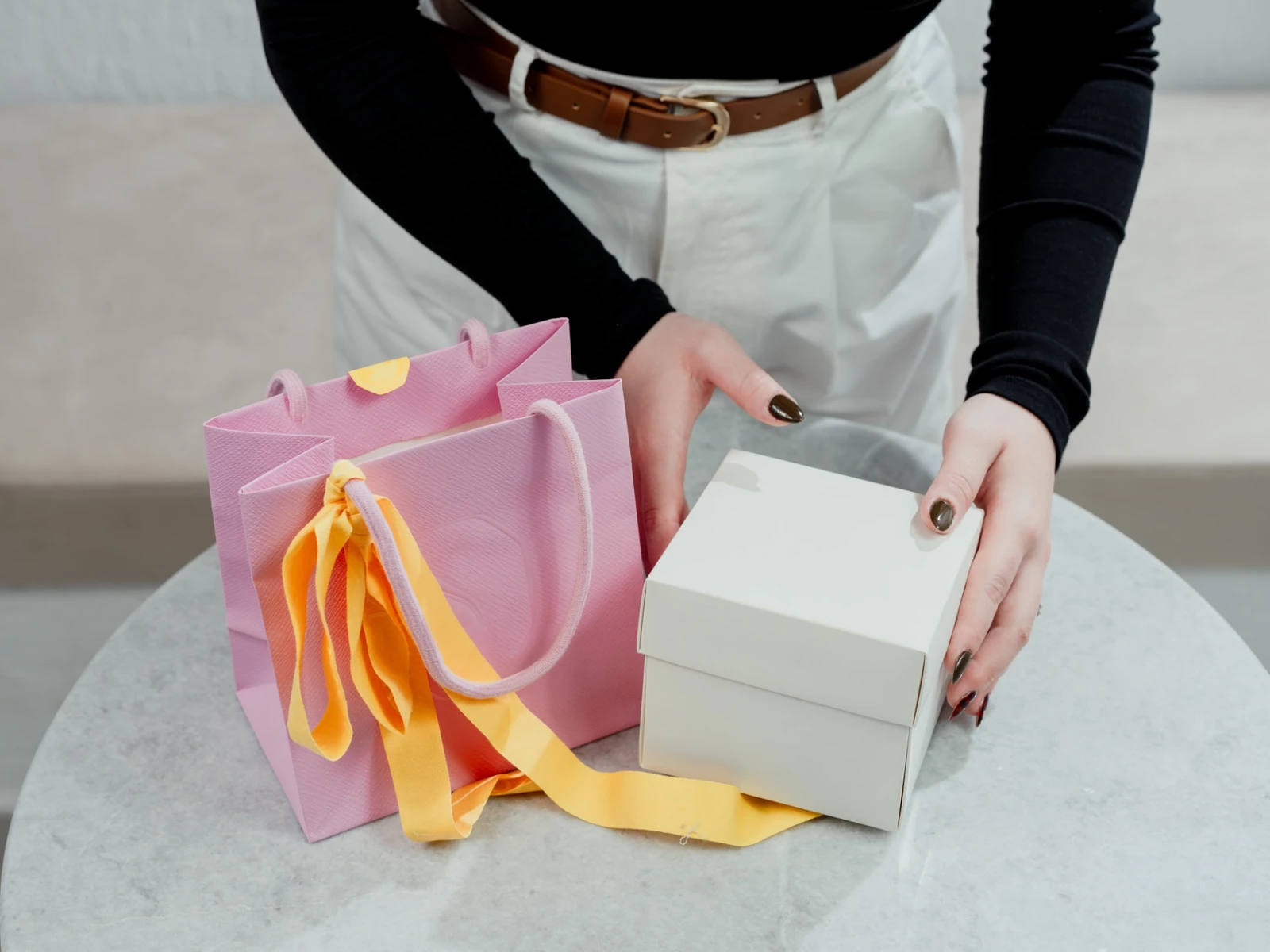 Pink paper gift bag with ribbon beside a white presentation box